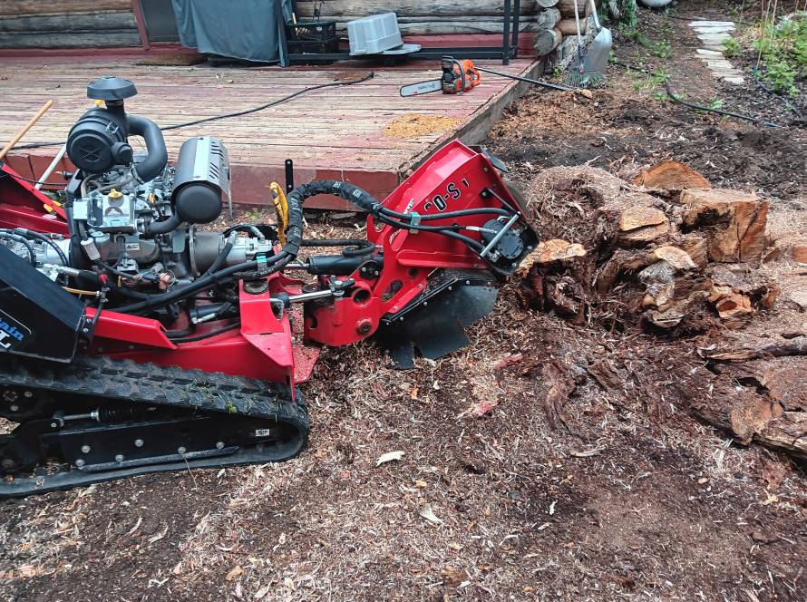 Close-up of stump grinding machine removing tree stump near log cabin deck in Jackson Hole, Wyoming